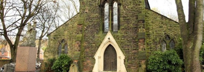 A photograph of the outside of Holy Trinity Church in Willenhall, West Midlands. A traditional stone church with large arched windows and doors.